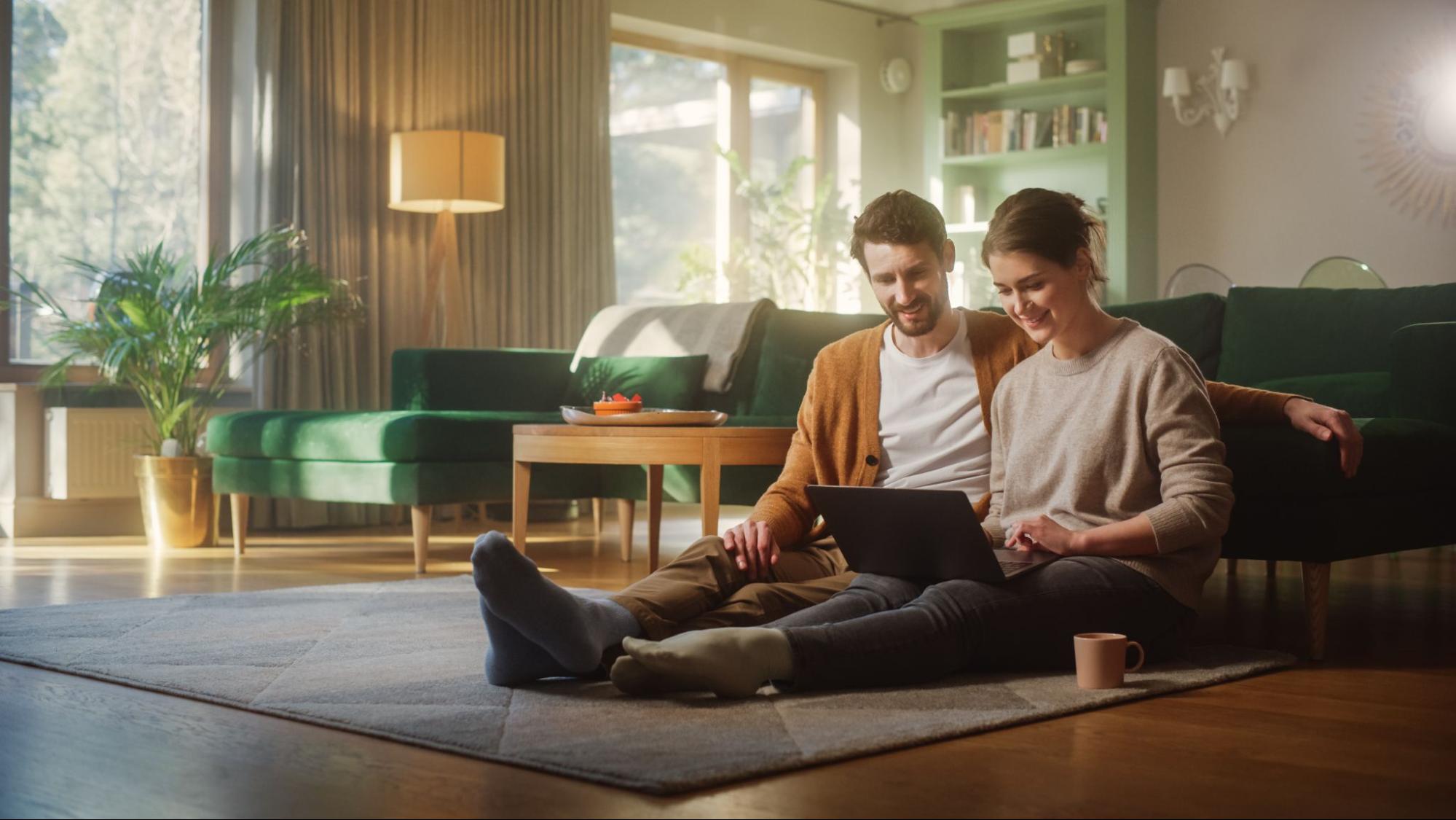A couple sitting on the floor looking at a laptop