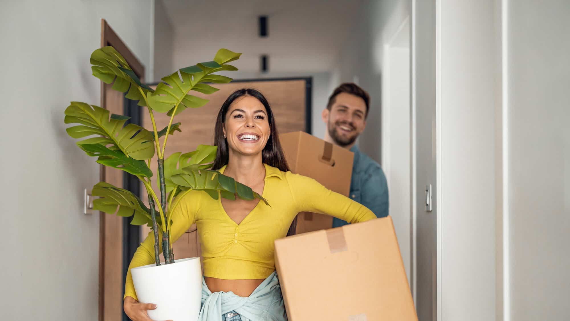 A couple carrying boxes and a plant into a home