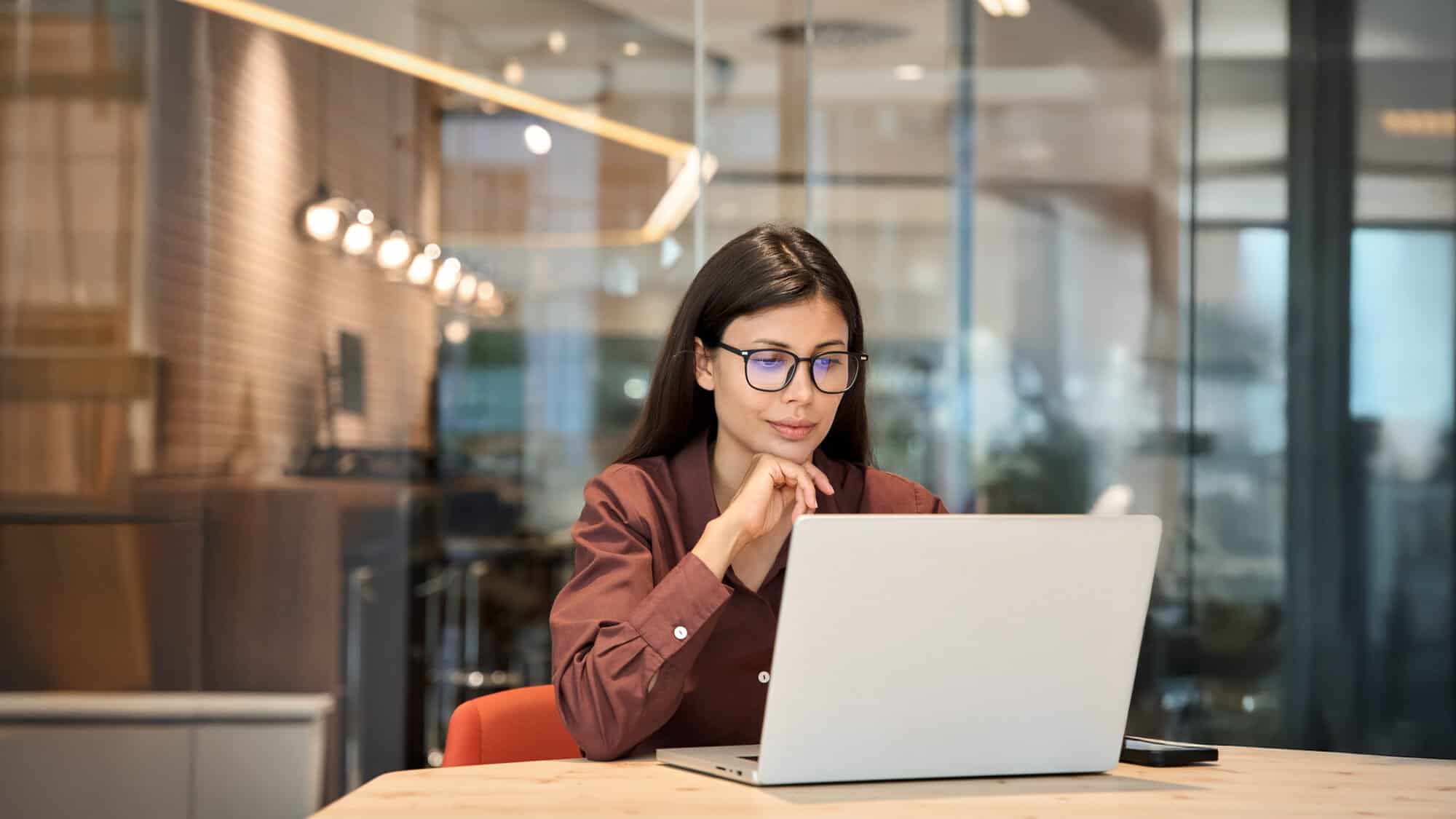 A woman with glasses looking at a laptop