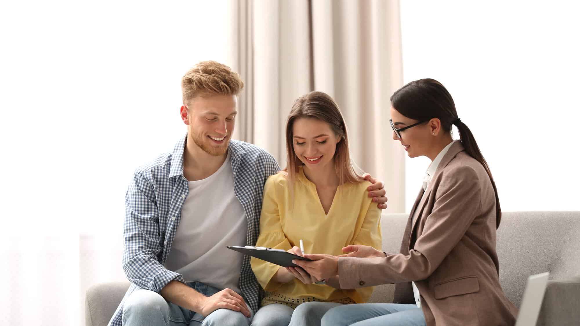 A couple on a couch signing paperwork with realtor