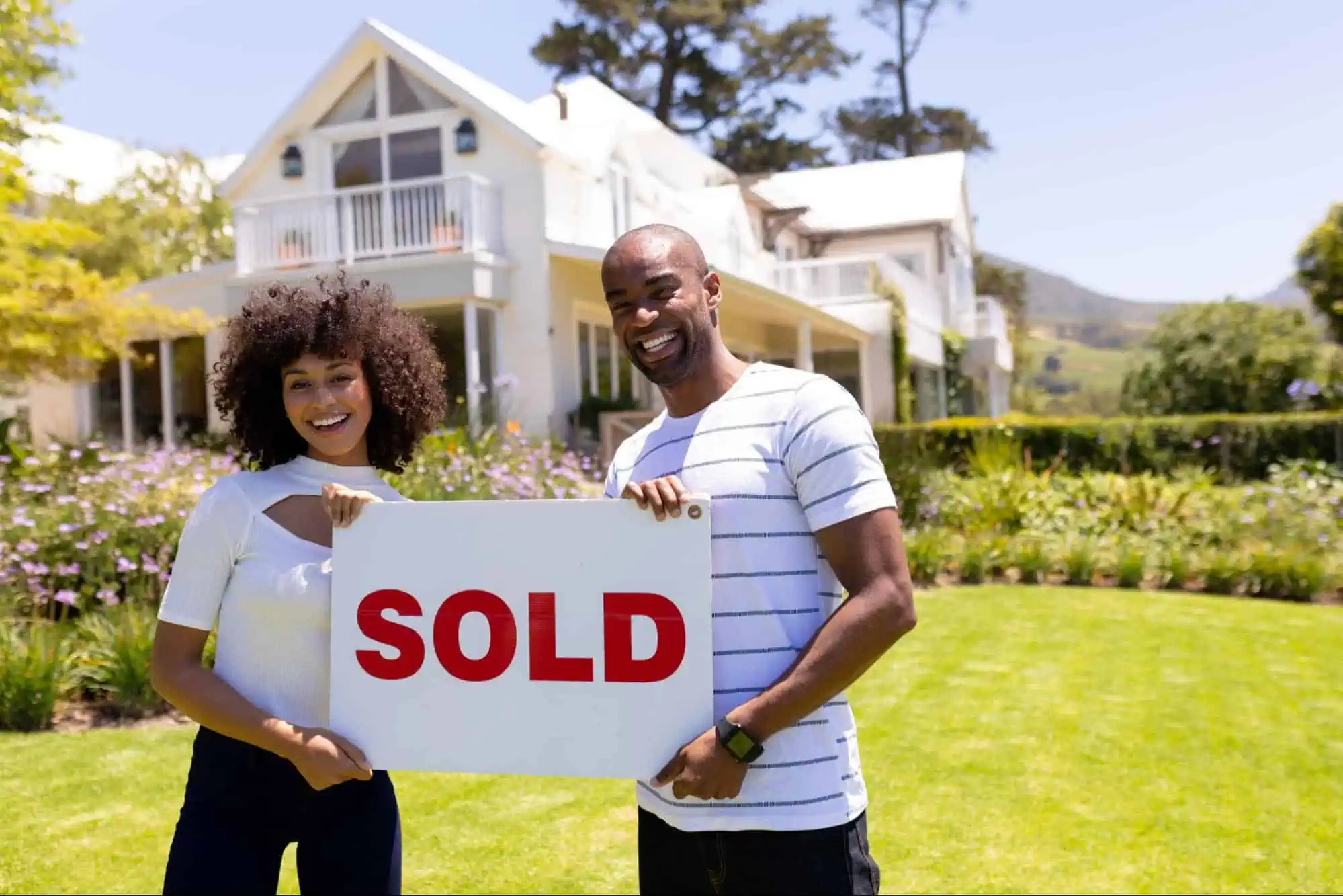 Couple holding a SOLD sign in front of house