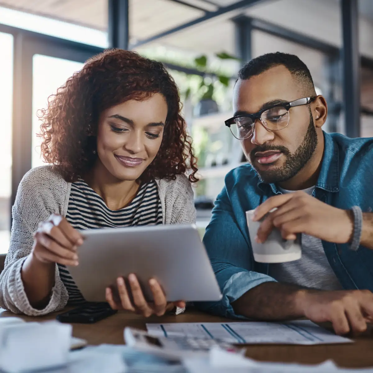 couple drinking coffee while holding a tablet